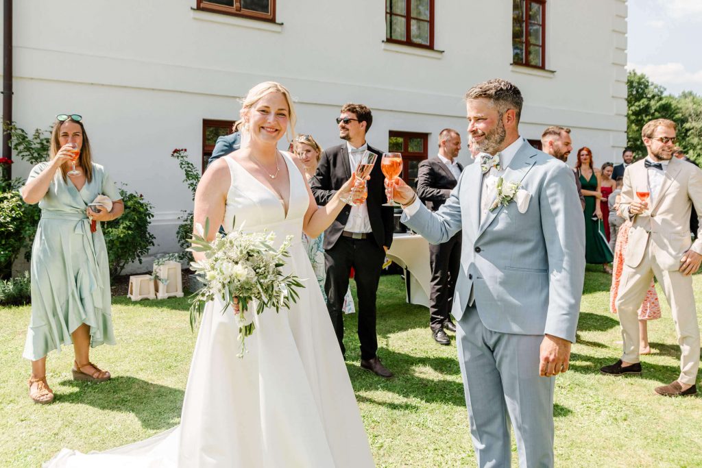 Brautpaar stößt mit Gästen im Garten an.