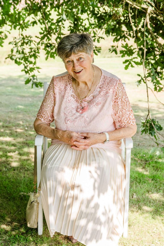 Ältere Frau sitzt im Garten auf Stuhl.