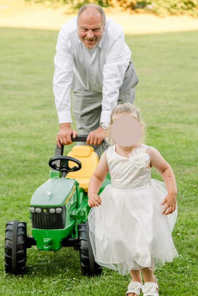 Mann spielt mit Kind auf Spielzeugtraktor Wiese