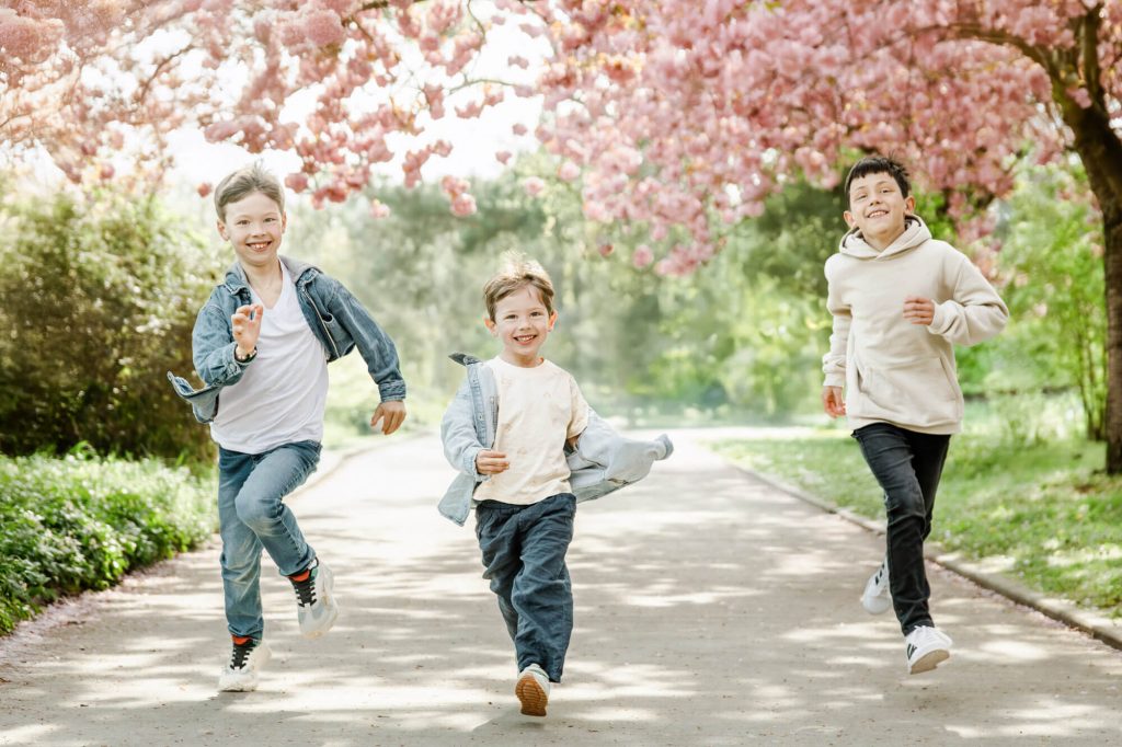 Drei lachende Jungen laufen unter blühenden Bäumen