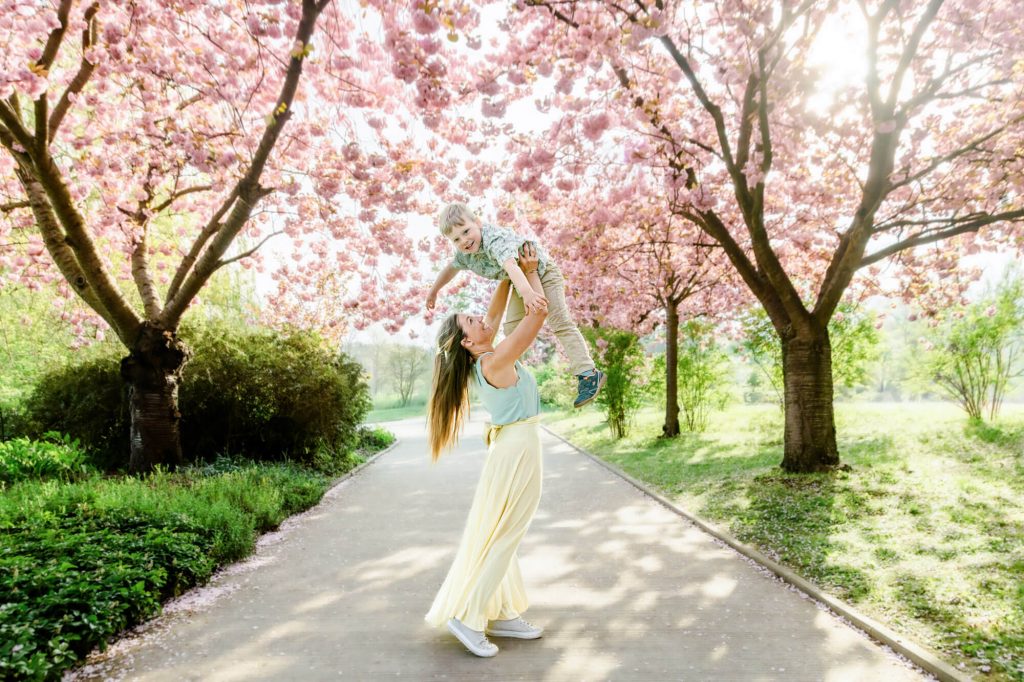 Frau hebt Kind auf blühender Kirschbaumallee
