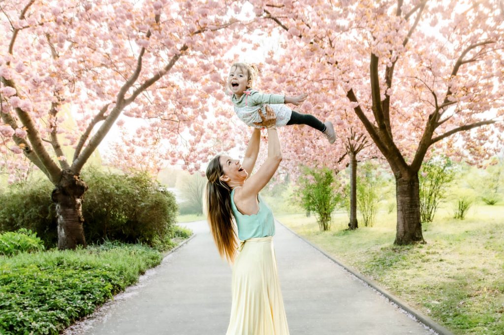Mutter hebt Kind im Kirschblütenpark hoch