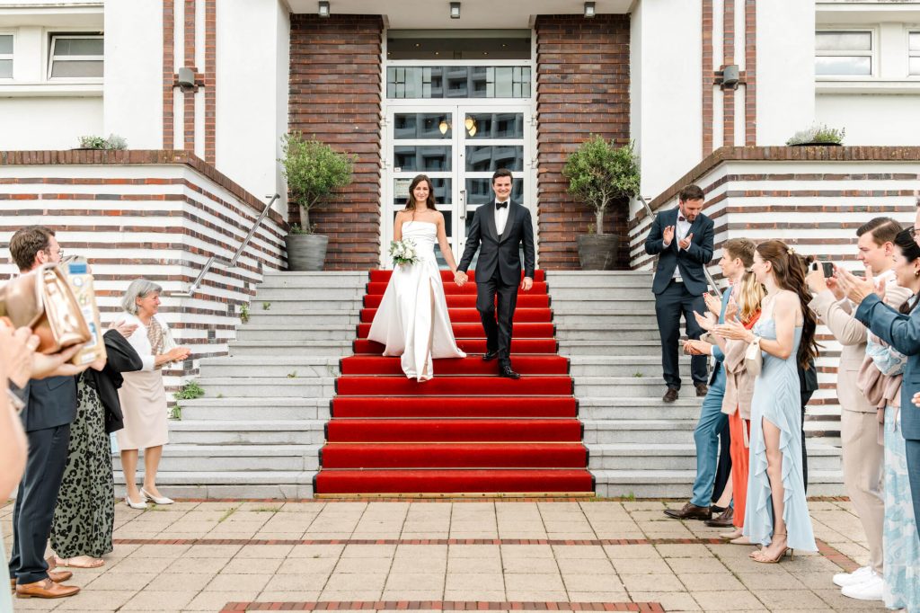 Hochzeitspaar auf rotem Teppich vor Gebäude