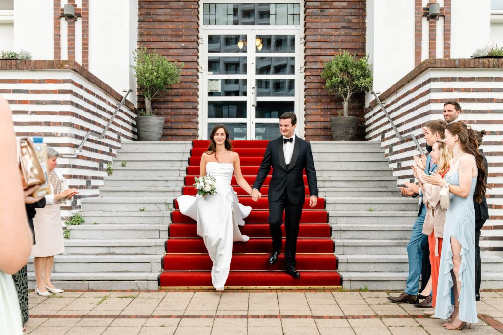 Brautpaar verlässt Kirche auf rotem Teppich glücklich