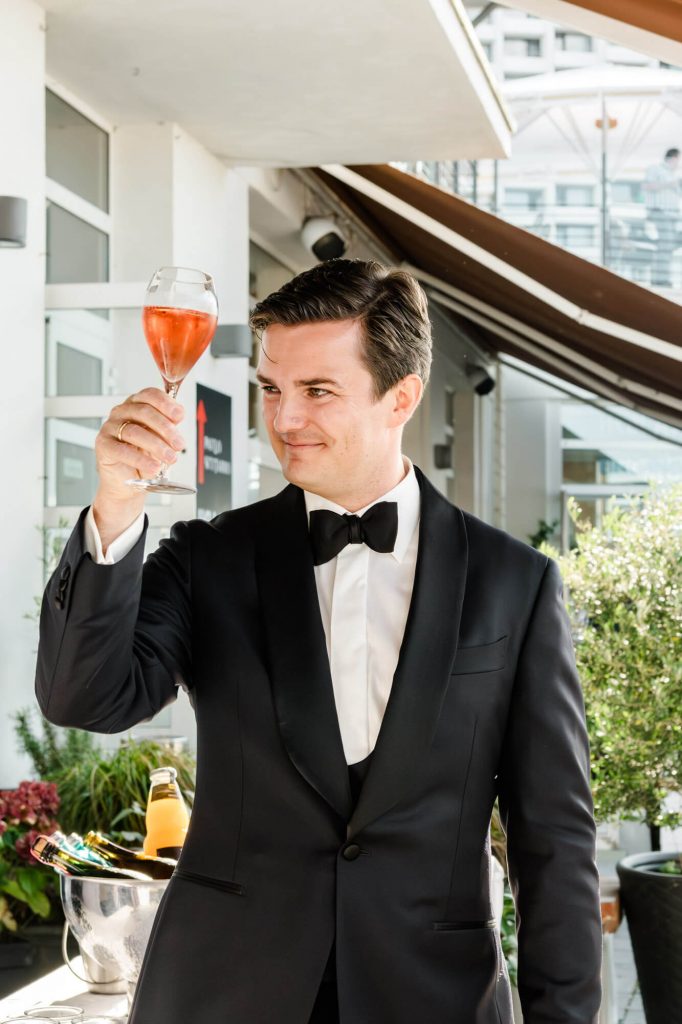 Mann im Smoking betrachtet ein Weinglas draußen