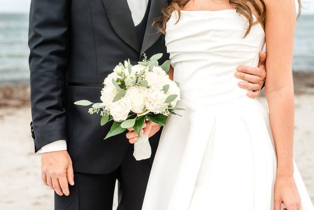 Brautpaar am Strand mit Blumenstrauß posiert