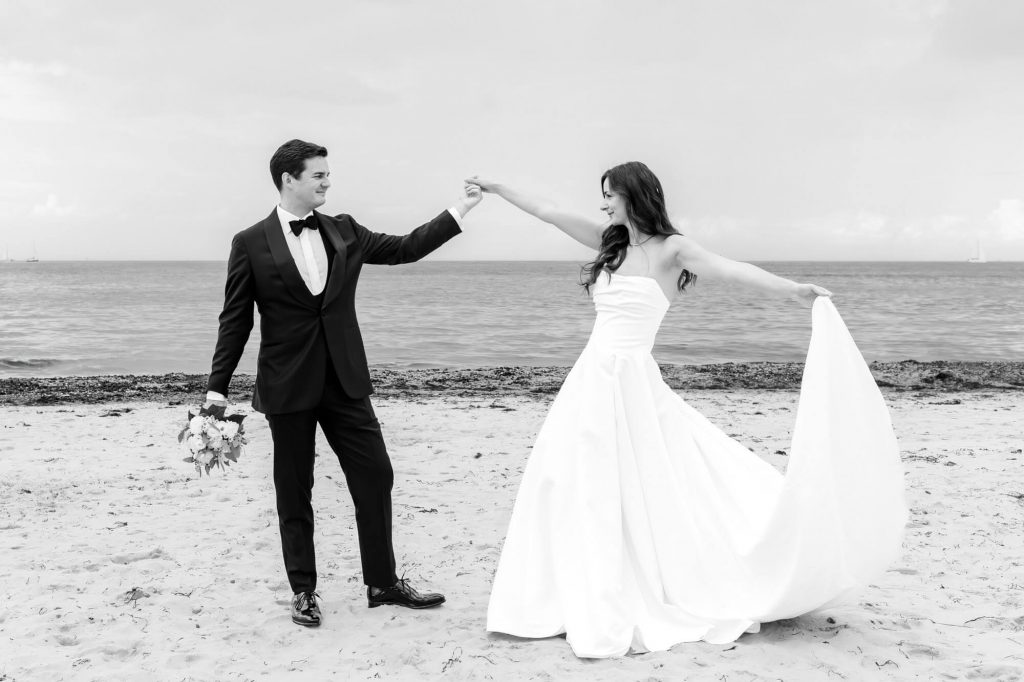 Brautpaar tanzt am Strand in Hochzeitskleidung.