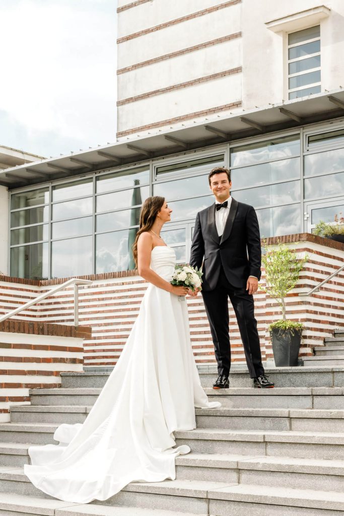 Brautpaar steht glücklich auf Hochzeitstreppe draußen