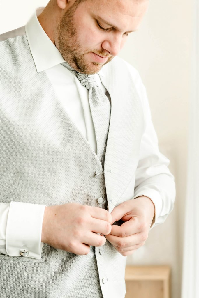 Mann in eleganter Weste knöpft sich zu.